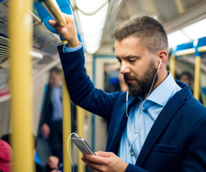 Serious businessman travelling to work. Standing inside underground wagon. Serious businessman with headphones travelling to work. Standing inside underground wagon, holding handhandle.