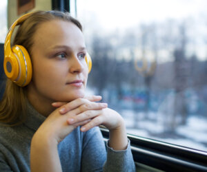 Woman traveling by train with favorite music Thoughtful young woman in the train listening to music in wireless headphones and enjoying passing landscape from the window