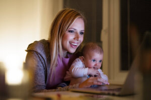 Mother with son in the arms, working on laptop Beautiful young mother at home at night with her little baby son in the arms, working on laptop